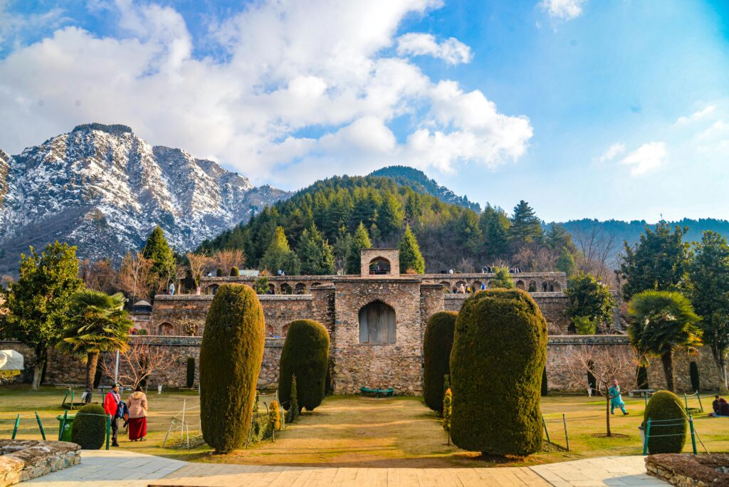 A stunning view of historical architecture set against snow-capped mountains and vibrant greenery.