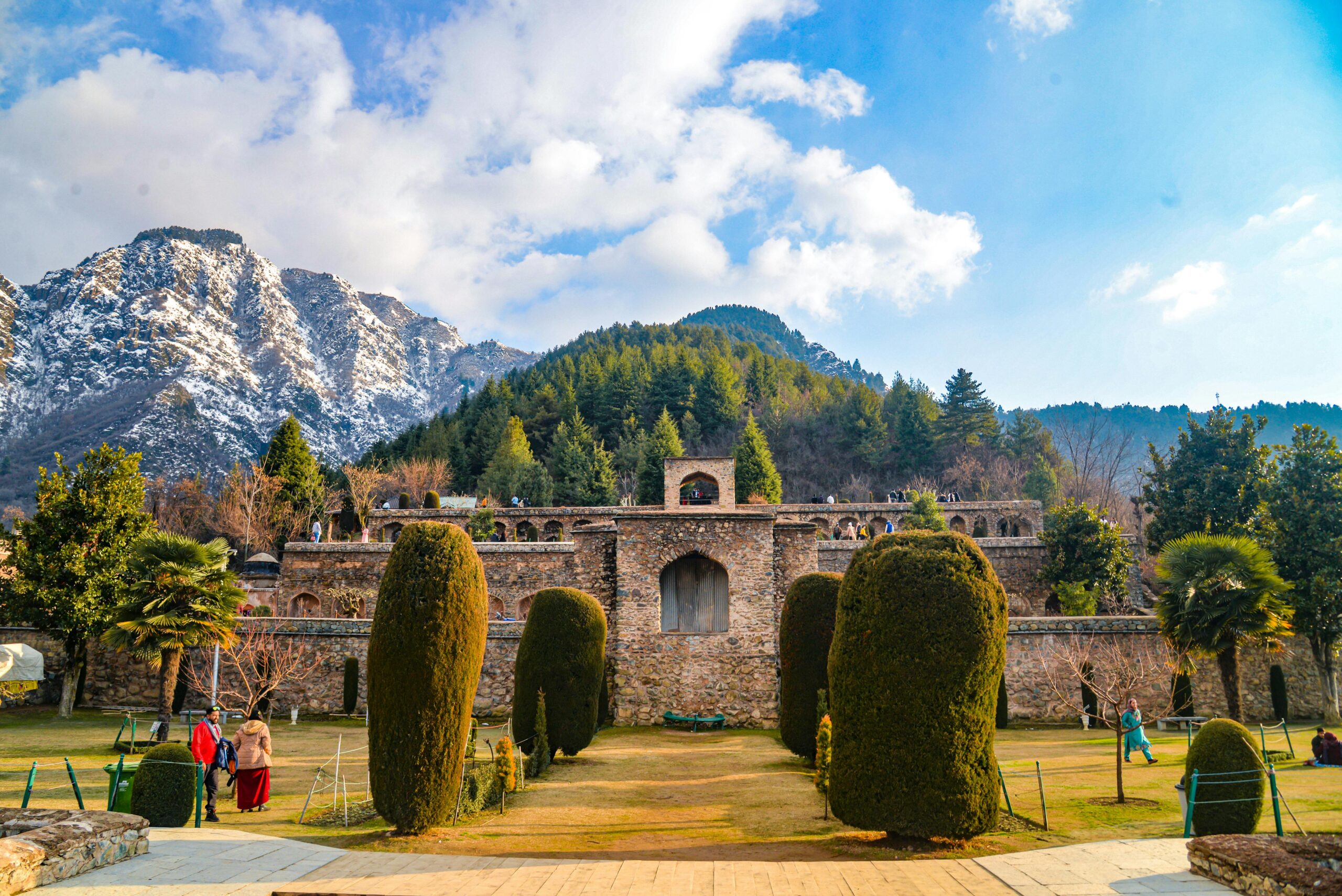 A stunning view of historical architecture set against snow-capped mountains and vibrant greenery.