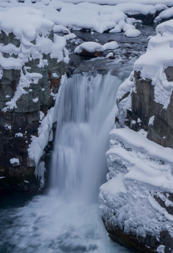 Stunning Aharbal waterfall flowing between snow-laden rocks in winter, showcasing nature's serene beauty.
