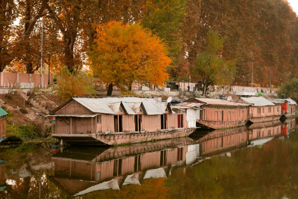 Rustic houseboats reflecting on a tranquil autumn river, surrounded by vibrant fall foliage.